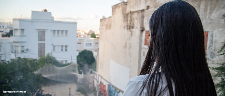 Woman looking out at Syrian landscape with broken buildings