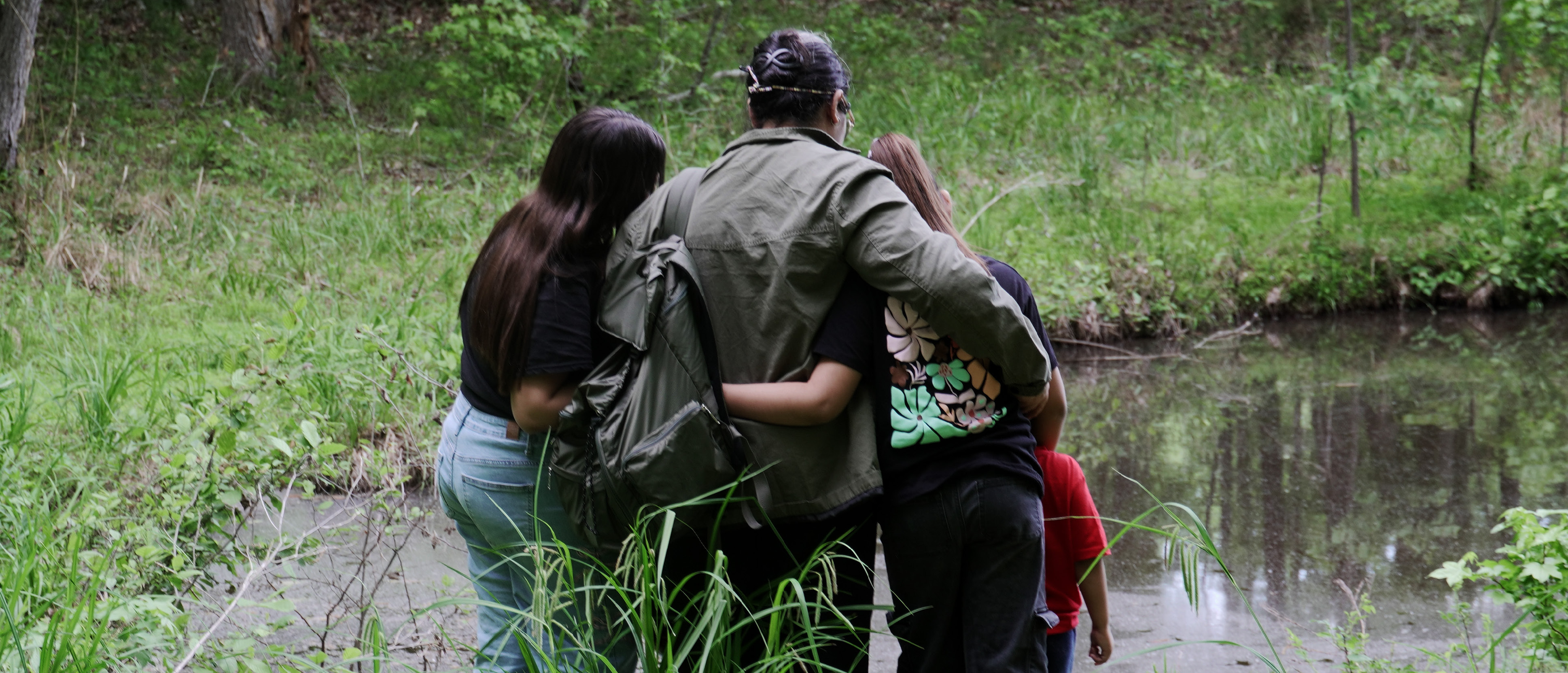 A family of four hug each other facing a lake