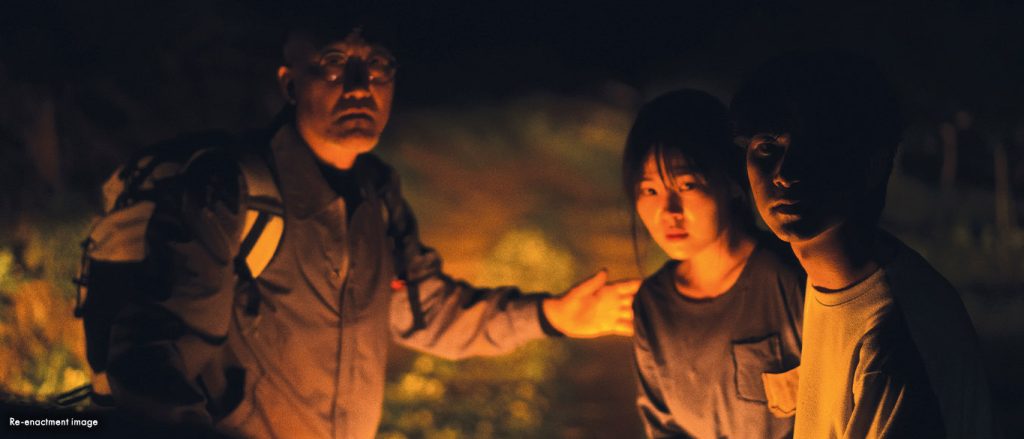 Three people stood around a campfire in a forest