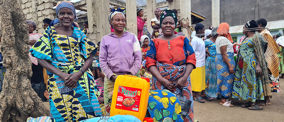 Three African women in dresses smile and hold bags