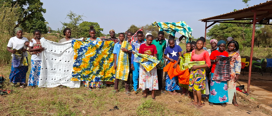 A group of Burkinabe people smile and hold colourful fabrics outside