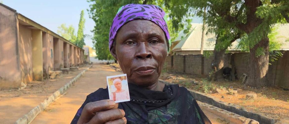 A Nigerian woman holds a photo and wears a purple headscarf.