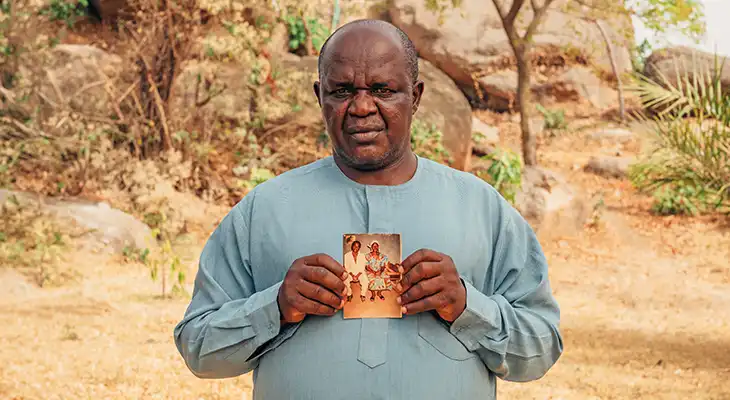 Pastor Josiah holds a picture of his martyred wife and son in front of a rocky backdrop.