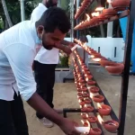 Man lights a candle and places it on a tray of other lit candles