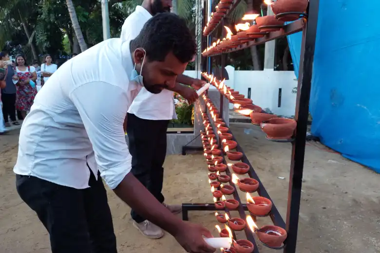 Man lights a candle and places it on a tray of other lit candles