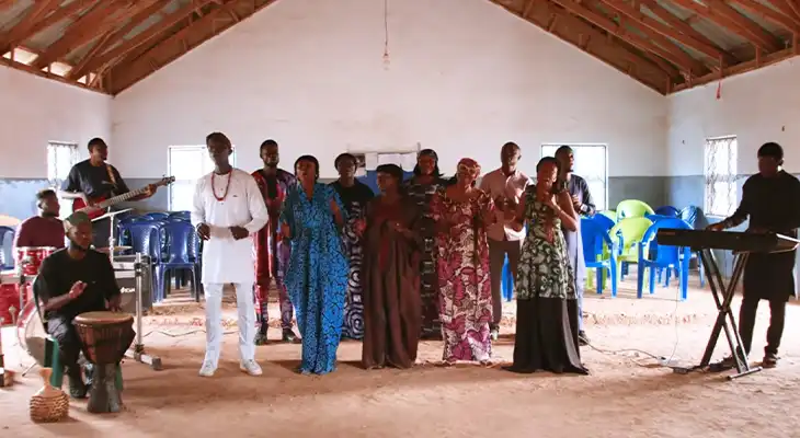 A group of singers with a pianist and a guitarist on either side stood in a building.