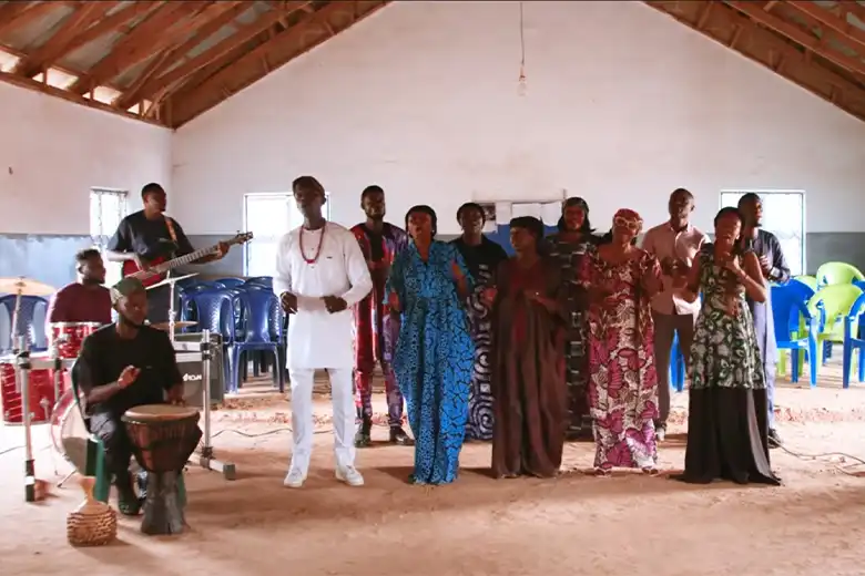 A group of singers with a pianist and a guitarist on either side stood in a building.