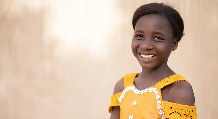 Aicha from Burkina Faso smiles and wears a yellow dress.