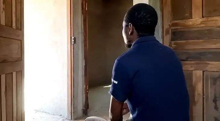 Ernesto looks out of an open doorway whilst sitting in a house.