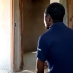Ernesto looks out of an open doorway whilst sitting in a house.