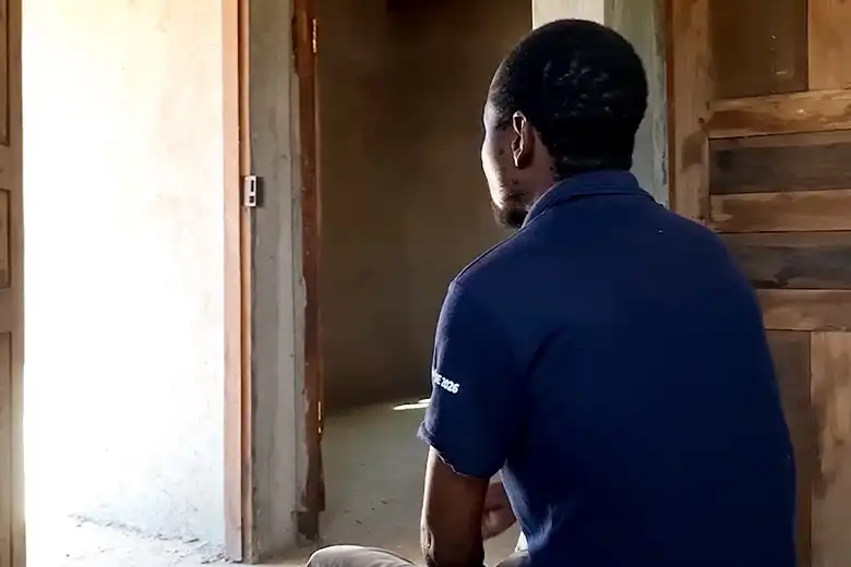 Ernesto looks out of an open doorway whilst sitting in a house.