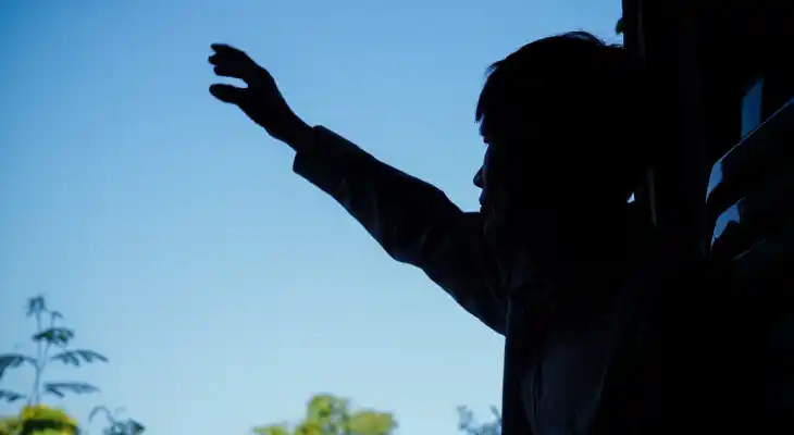 A man stood in shadows lifts his hands in prayer