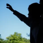 A man stood in shadows lifts his hands in prayer