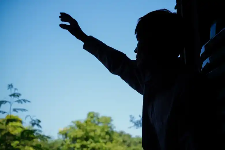 A man stood in shadows lifts his hands in prayer