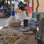 Ana from Mozambique sits at her marketplace stall with items she is selling on it.